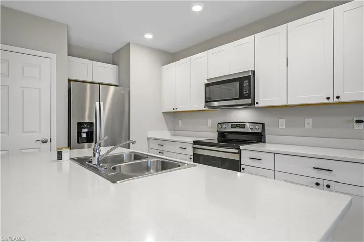 Kitchen with stainless steel appliances, white cabinets, recessed lighting, and light stone counters
