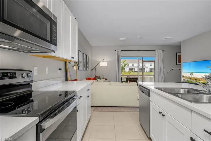 Kitchen with appliances with stainless steel finishes, white cabinets, open floor plan, light tile patterned floors, and light stone countertops