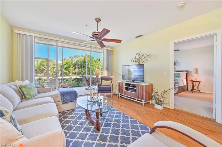 Living area with a ceiling fan, floor to ceiling sliding doors with view of the lake, and wood finished floors.