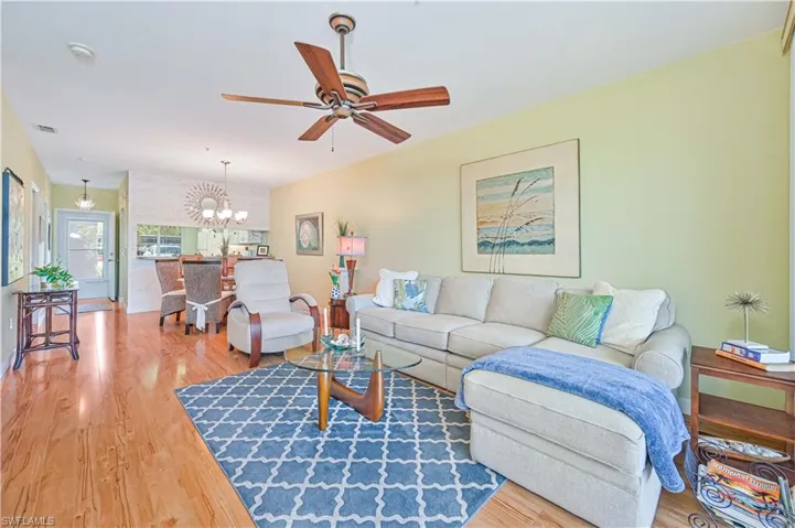 Living area with ceiling fan with notable chandelier, wood finished floors ,and lovely decor.