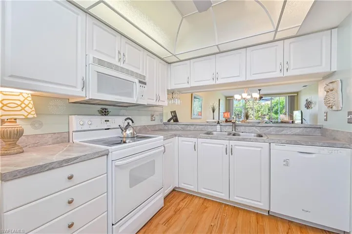 Kitchen with light countertops, white cabinetry, a sink, light wood-type flooring, and white appliances