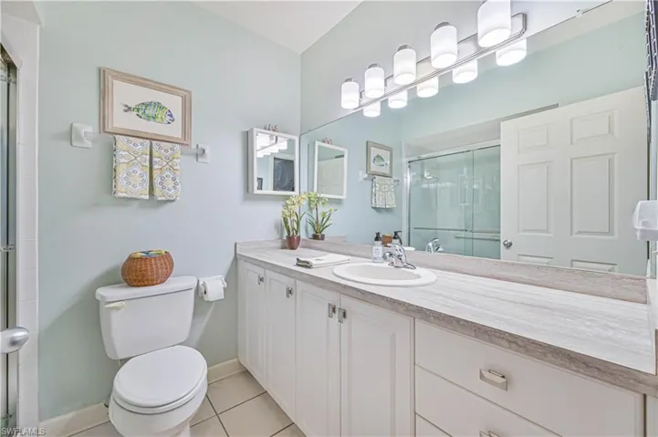 Full bath featuring toilet, a shower with shower door, vanity, baseboards, and tile patterned floors