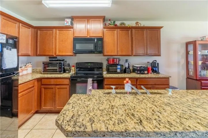 Kitchen with a toaster, light tile patterned floors, a sink, light stone countertops, and black appliances