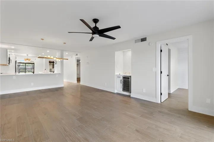 Unfurnished living room with wine cooler, light wood-style floors, ceiling fan, and a chandelier