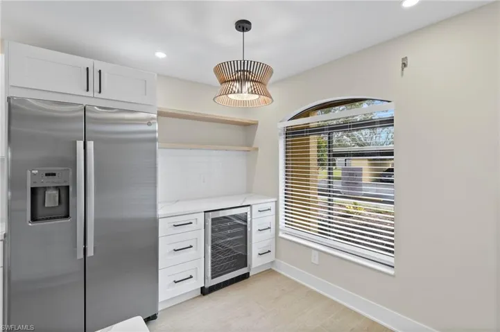 Bar with stainless steel refrigerator with ice dispenser, open shelves, light stone countertops, wine cooler, and backsplash