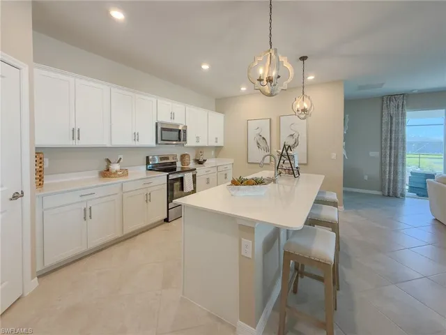 Kitchen with appliances with stainless steel finishes, an island with sink, a kitchen breakfast bar, white cabinets, and pendant lighting