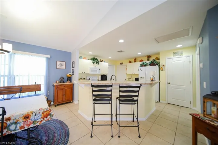 Kitchen featuring a kitchen breakfast bar, a center island with sink, white appliances, and lofted ceiling