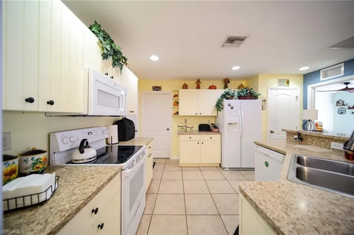 Kitchen featuring light tile patterned flooring, light stone countertops, sink, and white appliances.