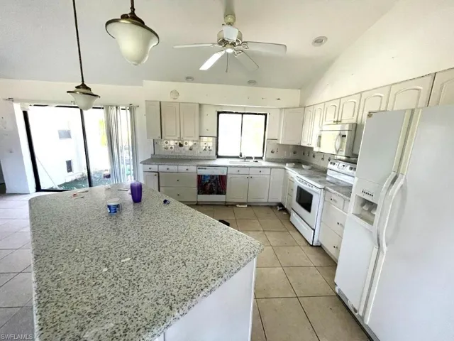 Kitchen featuring a large central island with a speckled countertop, white cabinetry, a complete suite of white appliances, tile flooring, and vaulted ceilings with a ceiling fan