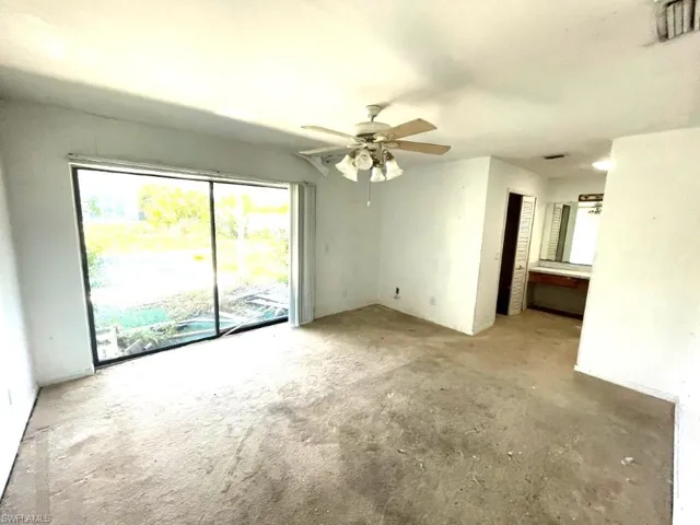 Expansive room featuring large sliding glass doors, a ceiling fan with integrated lighting, a built-in vanity with mirror, and neutral wall finishes