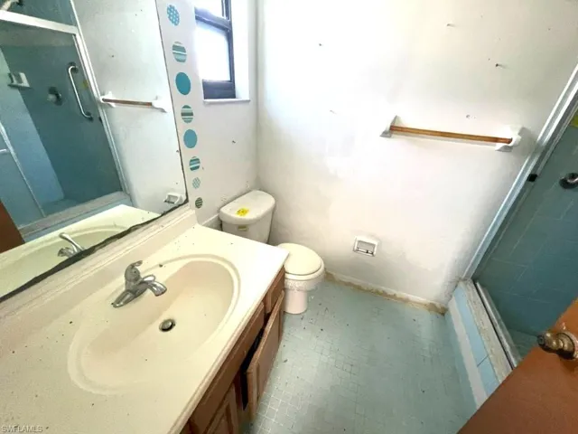 Bathroom featuring a single vanity with an integrated sink, a wall-mounted mirror, a toilet, a shower stall with a glass enclosure, and tiled flooring