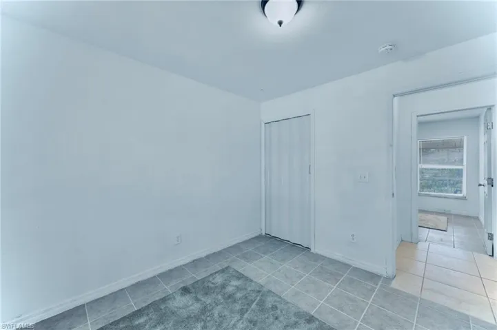Empty room with a smoke detector, light tile patterned flooring, and baseboards