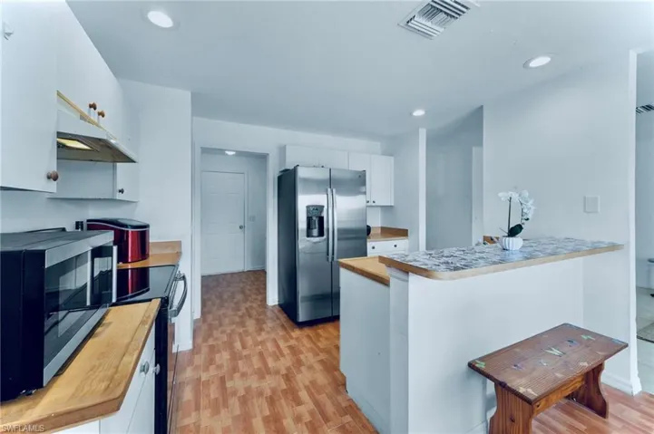 Kitchen with appliances with stainless steel finishes, under cabinet range hood, a peninsula, butcher block counters, and white cabinetry