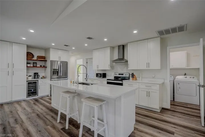 Kitchen with white cabinetry, wall chimney exhaust hood, sink, and stainless steel appliances