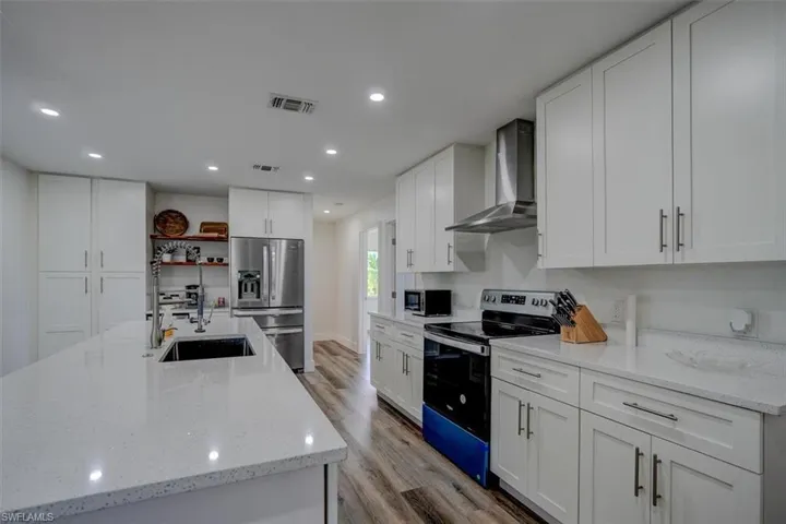 Kitchen featuring electric range oven, wall chimney exhaust hood, sink, white cabinets, and stainless steel fridge with ice dispenser