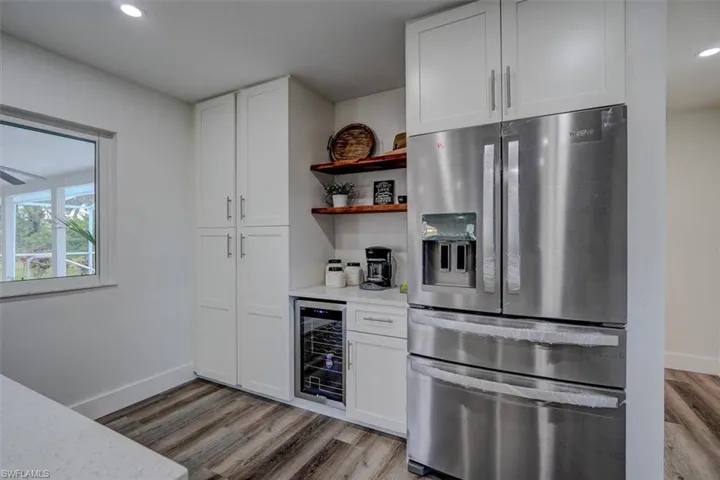 Kitchen featuring stainless steel refrigerator with ice dispenser, wine cooler, light stone counters, light hardwood / wood-style floors, and white cabinetry