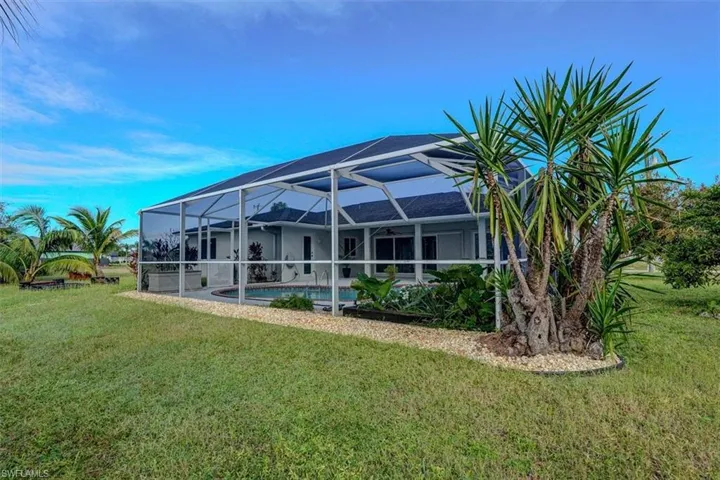 Back of property featuring a lawn and glass enclosure