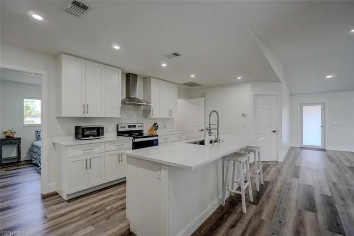 Kitchen with white cabinetry, an island with sink, wall chimney range hood, and appliances with stainless steel finishes