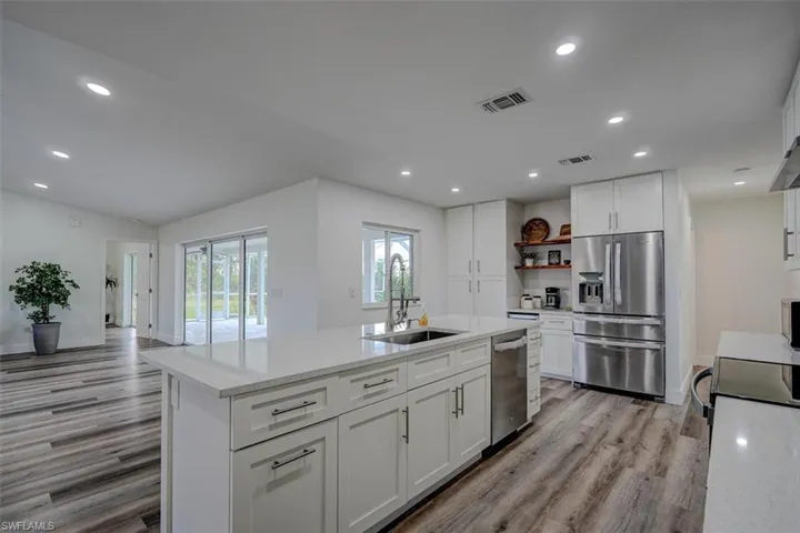 Kitchen with sink, light stone counters, light hardwood / wood-style floors, white cabinets, and appliances with stainless steel finishes