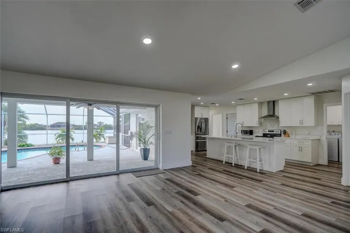 Kitchen with range with electric cooktop, plenty of natural light, wall chimney exhaust hood, and an island with sink