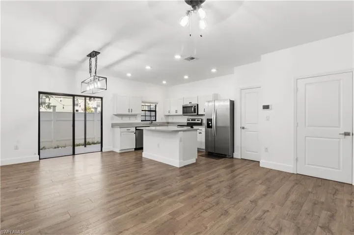 Kitchen with open floor plan, stainless steel appliances, white cabinets, a kitchen island, and a ceiling fan