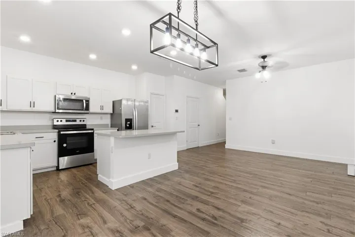 Kitchen featuring pendant lighting, stainless steel appliances, a kitchen island, white cabinets, and open floor plan