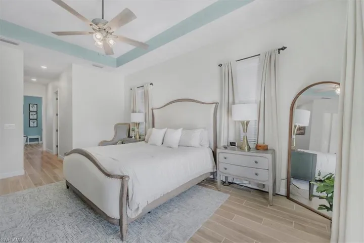 Bedroom with a tray ceiling, wood tiled floors, and a ceiling fan