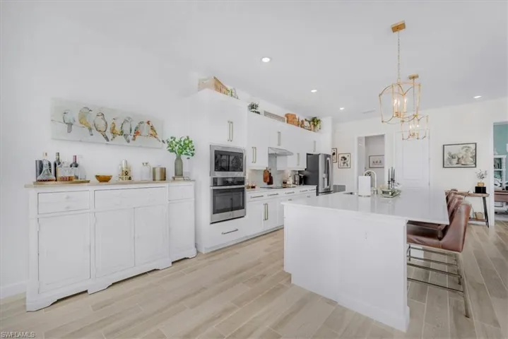 Kitchen with white cabinets, a kitchen breakfast bar, a center island with sink, pendant lighting, and wood tiled floors