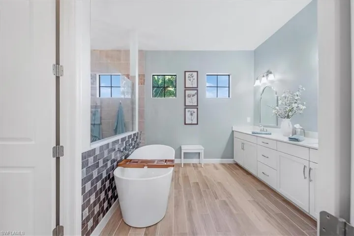 Bathroom with walk in shower, double vanity, wood finish floors, and a freestanding bath