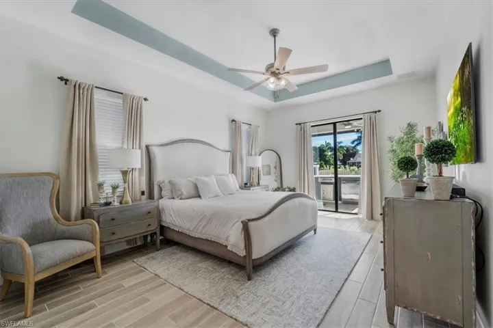 Bedroom with a tray ceiling, access to outside, wood tiled floors, and a ceiling fan