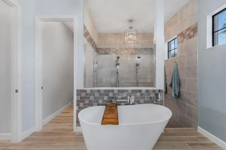 Full bath featuring tile walls, wood tiled floors, a walk in shower, a freestanding bath, and a chandelier