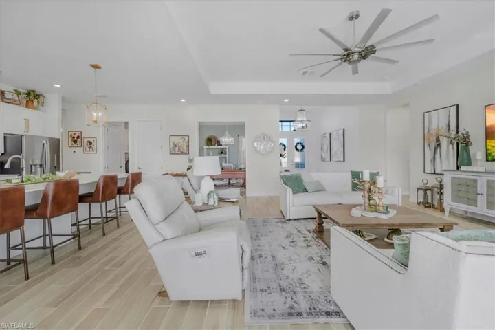 Living room with a chandelier, light wood-type flooring, a raised ceiling, recessed lighting, and ceiling fan