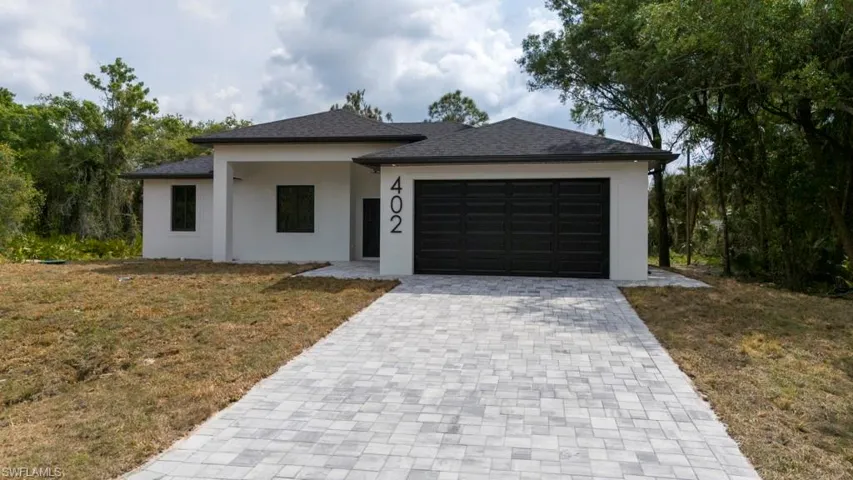 View of front of home with a front yard, stucco siding, an attached garage, a shingled roof, and decorative driveway