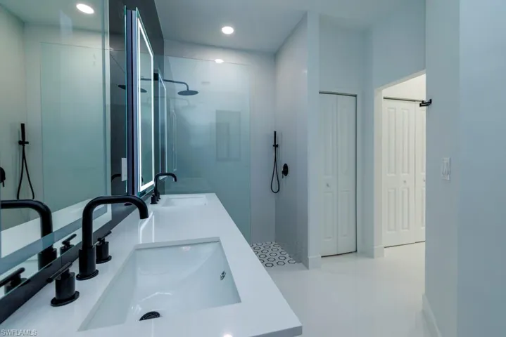 Full bath featuring double vanity, recessed lighting, tiled shower, and a sink