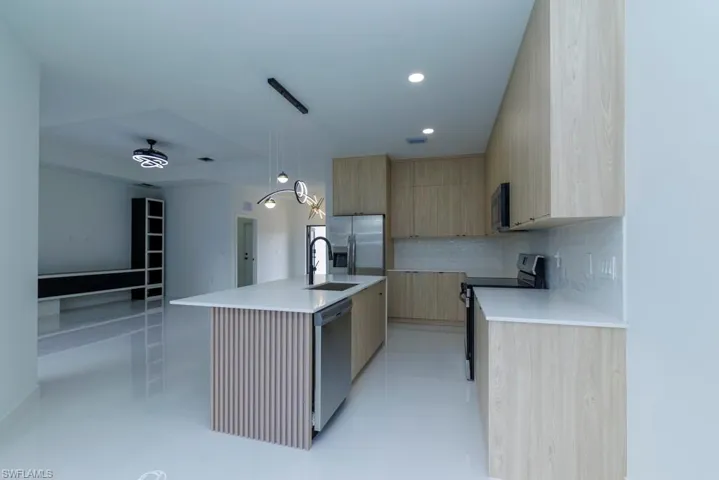 Kitchen with light countertops, light brown cabinetry, backsplash, modern cabinets, and appliances with stainless steel finishes
