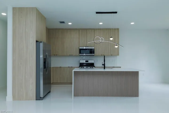 Kitchen featuring light countertops, a sink, light brown cabinetry, appliances with stainless steel finishes, and modern cabinets