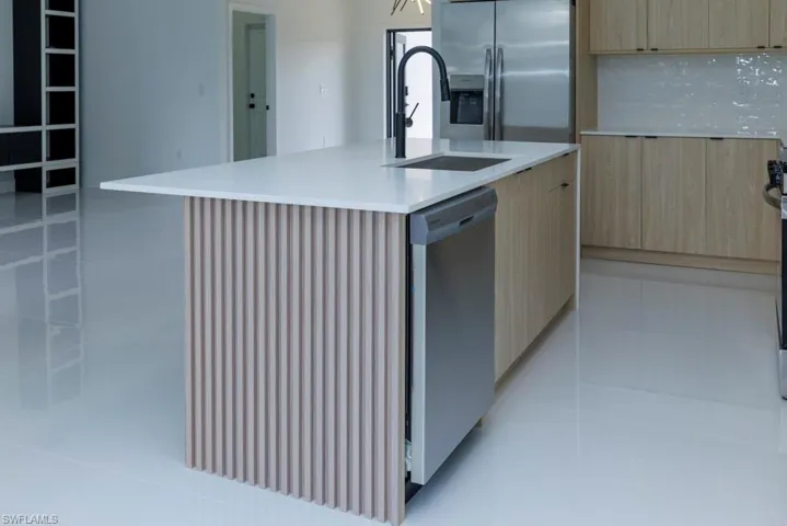 Kitchen with modern cabinets, a sink, light brown cabinetry, and appliances with stainless steel finishes