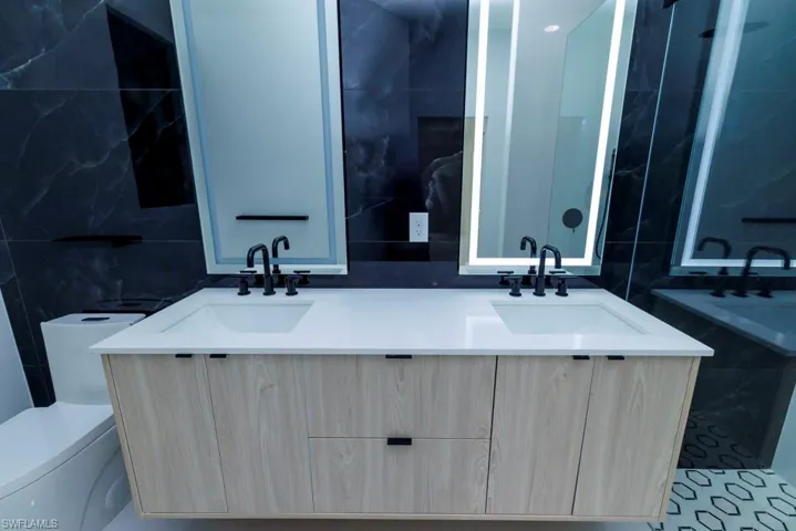 Bathroom with double vanity, toilet, tile walls, and a sink
