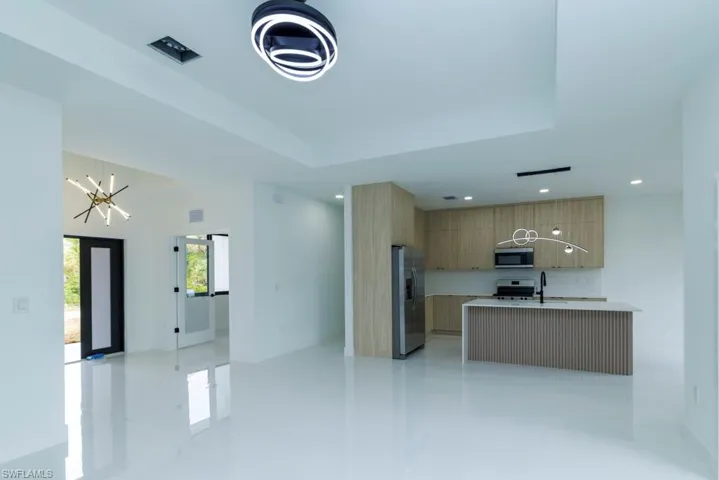 Kitchen featuring light countertops, modern cabinets, a raised ceiling, appliances with stainless steel finishes, and a notable chandelier