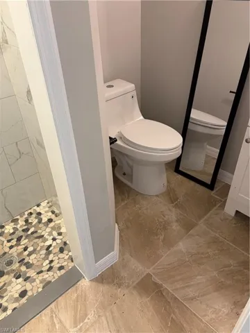 Bathroom featuring a modern toilet, large format floor tiling, a river rock shower floor, and marble-look shower wall tiling