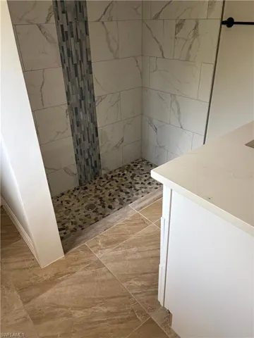 Walk-in shower featuring large format veined wall tiles, a vertical mosaic accent, and a river rock floor