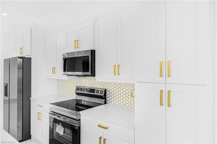 Kitchen featuring light stone counters, stainless steel appliances, decorative backsplash, and white cabinets