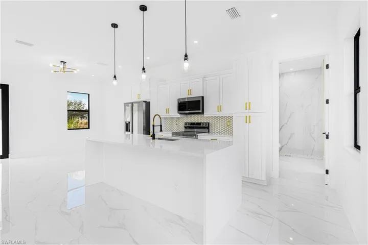 Kitchen with white cabinetry, stainless steel appliances, decorative light fixtures, and a kitchen island with sink