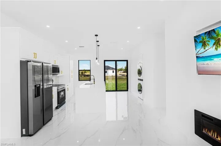 Kitchen with stainless steel appliances, white cabinetry, sink, and decorative light fixtures