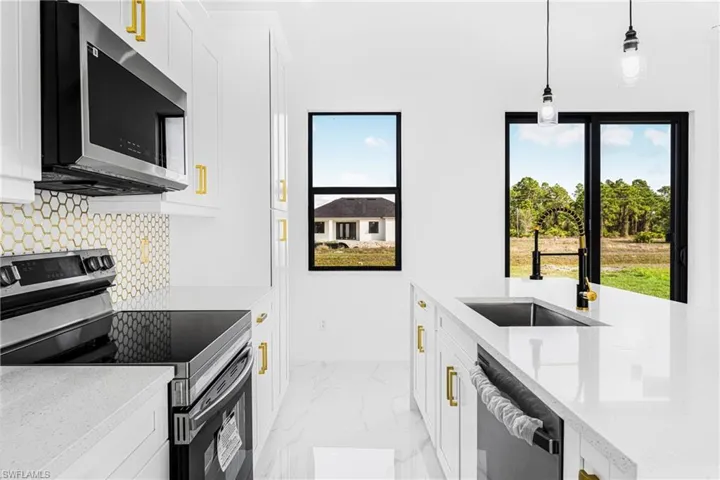 Kitchen with pendant lighting, white cabinetry, sink, stainless steel appliances, and light stone countertops