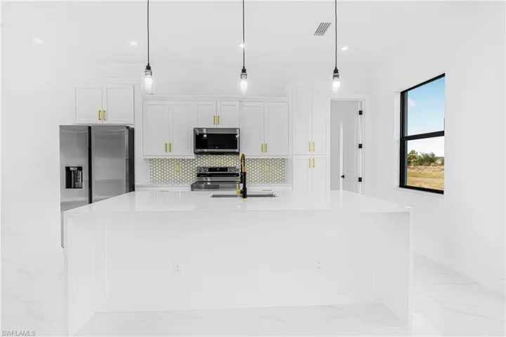 Kitchen featuring white cabinetry, decorative light fixtures, a center island with sink, and appliances with stainless steel finishes