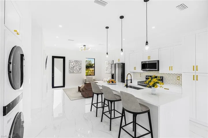 Kitchen with sink, white cabinetry, a center island with sink, appliances with stainless steel finishes, and stacked washer / dryer