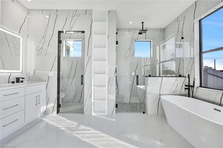 Full bath featuring a freestanding bath, light marble finish floors, a marble finish shower, plenty of natural light, and recessed lighting