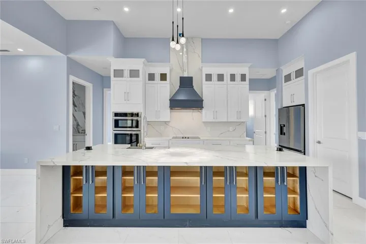 Kitchen featuring glass insert cabinets, light stone countertops, a large island, stainless steel appliances, and white cabinetry