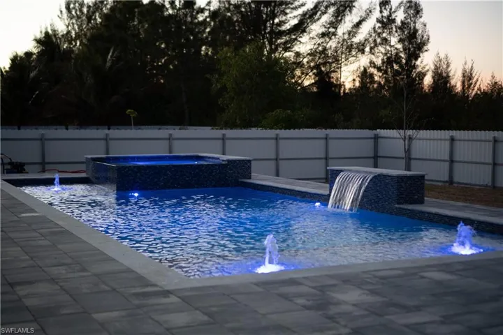 Pool at dusk featuring a fenced backyard and a pool with connected hot tub